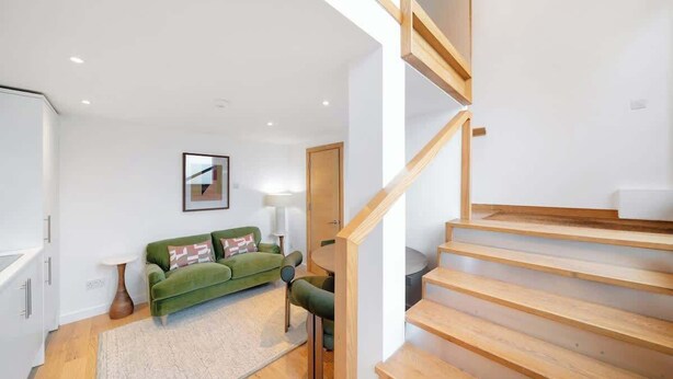 A modern interior with a staircase, a green sofa, and a white cabinet. - Fulham Split-Level 1-Bed Studio | Sleeps 4 (Greater London)