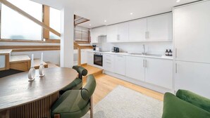 A modern kitchen with white cabinets, a dining area with a round table and chairs, and a staircase leading to an upper level. - Fulham Split-Level 1-Bed Studio | Sleeps 4 (Greater London)