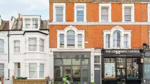 A building with a shop named 'The Grooming Lounge' on the ground floor, a number 99 sign above the entrance, and a bicycle parked outside. - Fulham Split-Level 1-Bed Studio | Sleeps 4 (Greater London)