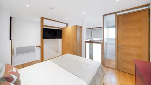 A bedroom with a bed, a TV mounted on the wall, a wardrobe, and a sliding glass door. - Fulham Split-Level 1-Bed Studio | Sleeps 4 (Greater London)