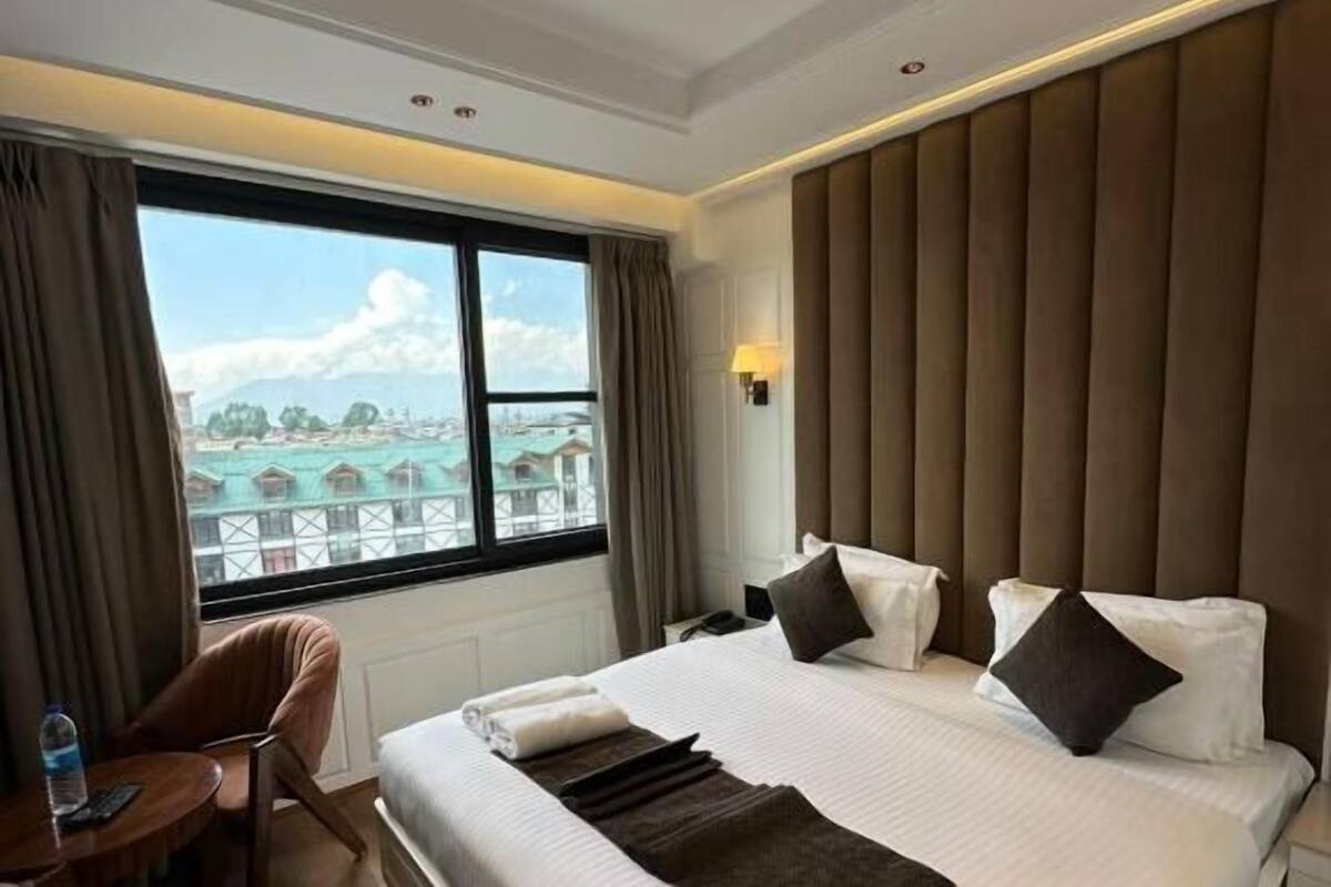 Quarto de hotel com uma cama grande, uma mesa, uma cadeira e vista para prédios pela janela.