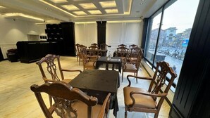 A spacious room with a large dining table surrounded by chairs, a black cabinet, and a view of the city through large windows. - HOTEL LA SERA (Srinagar)