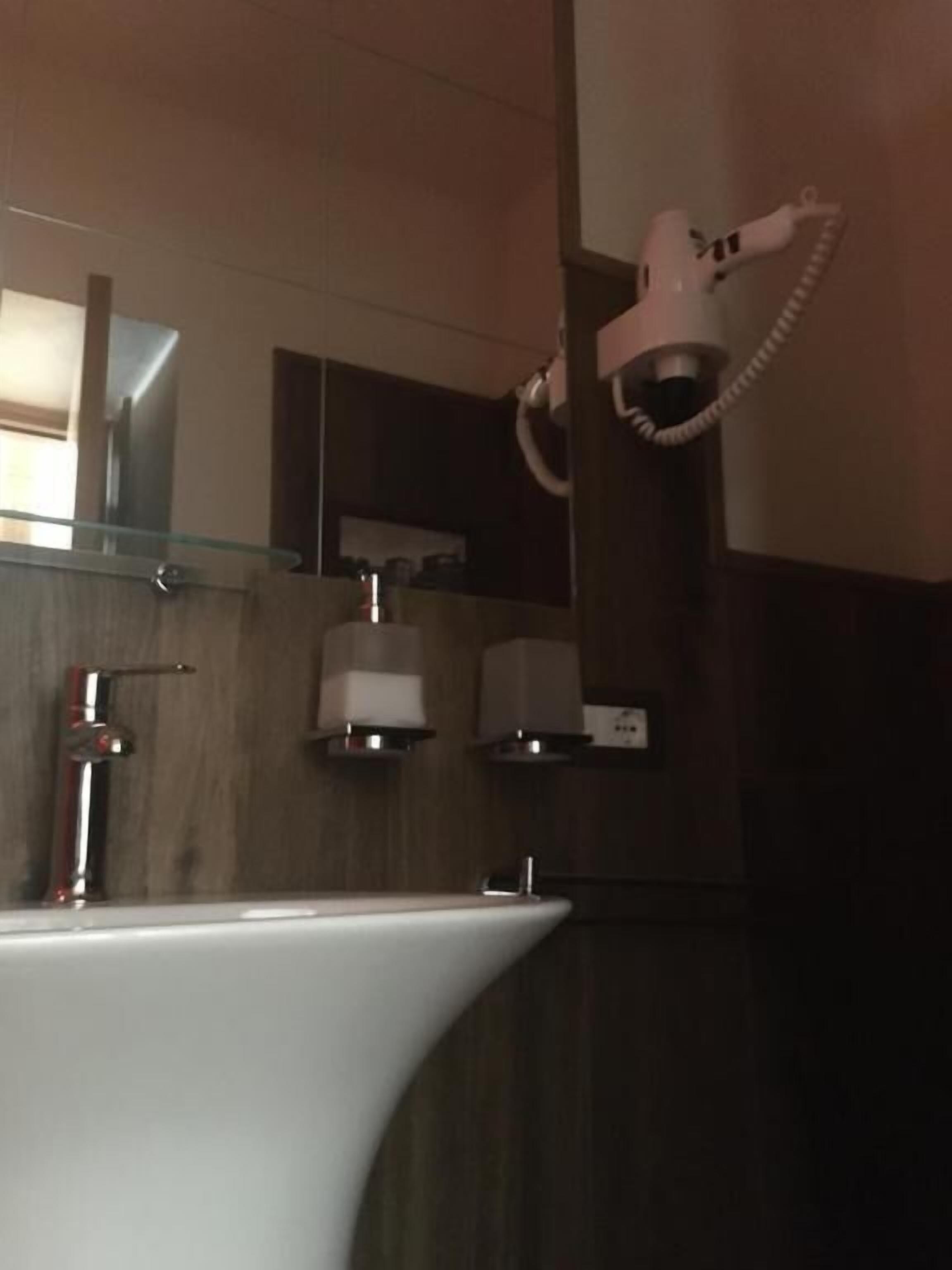 Un baño con lavamanos blanco, un espejo, secador de pelo y toallero.
