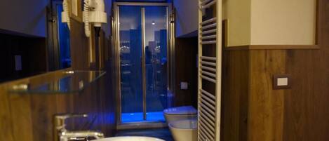 A modern bathroom with a glass shower enclosure, a white sink, and a towel rack.
