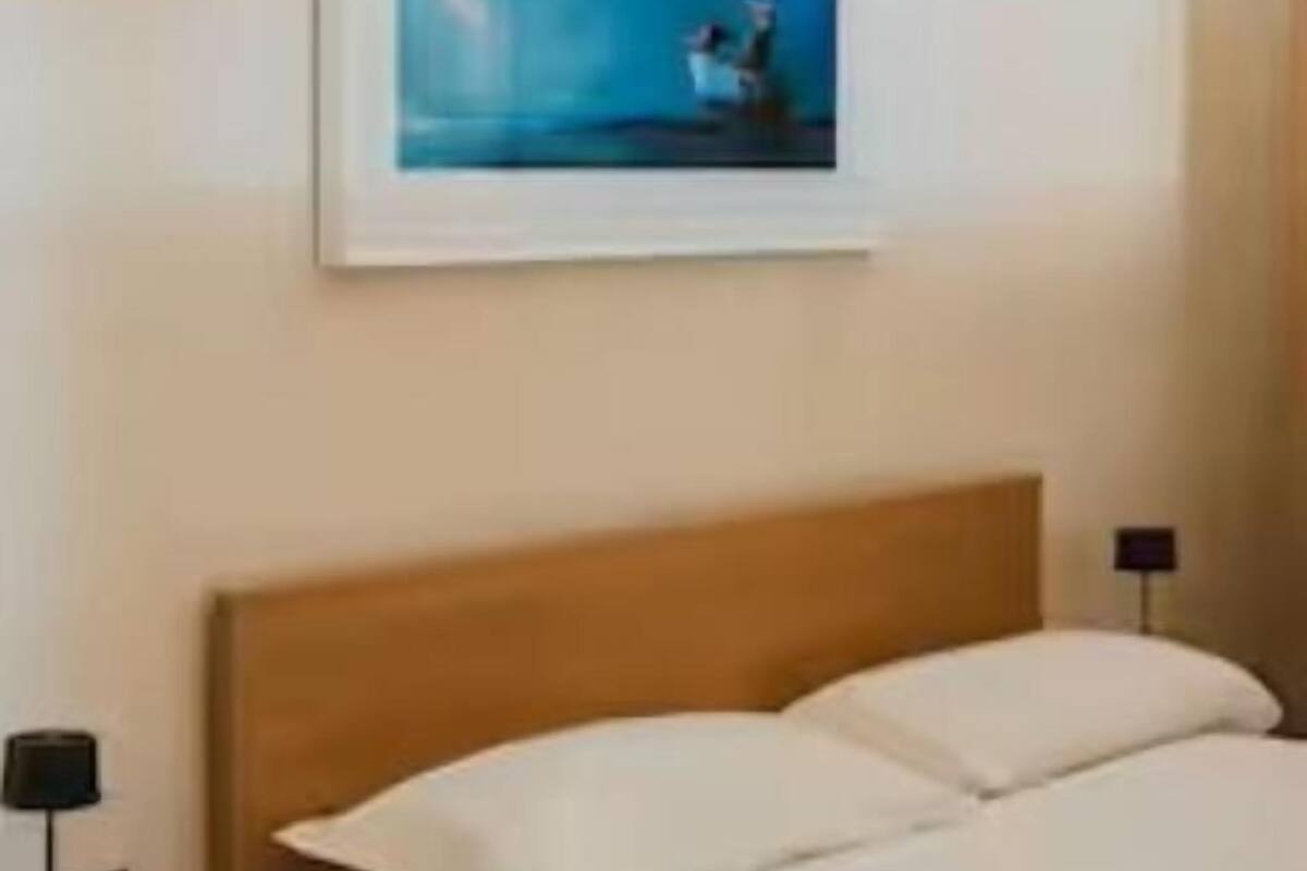 A hotel room with a bed, a nightstand, a lamp, and a framed picture on the wall.