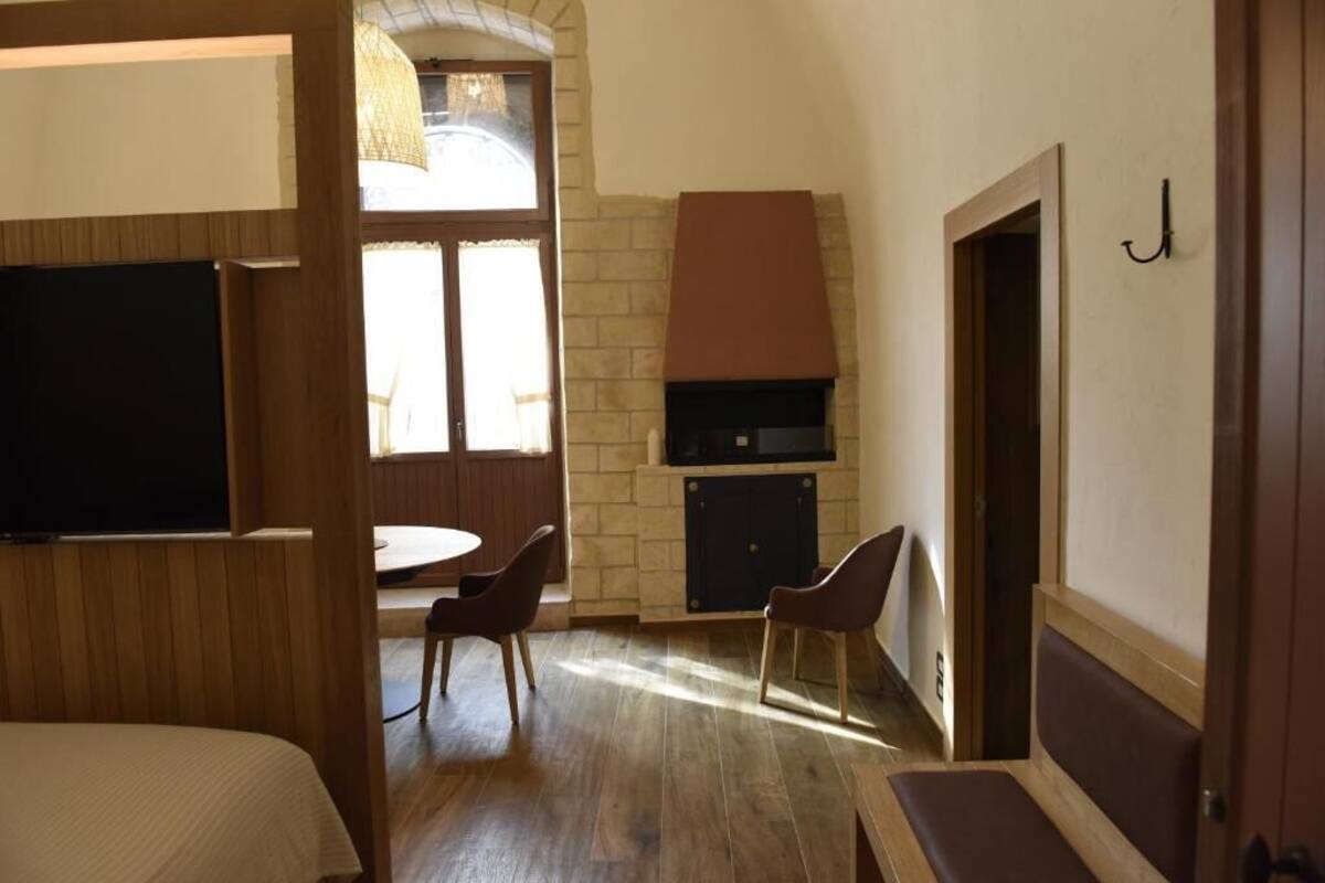A room with a bed, a TV, a fireplace, a dining area with chairs, and a view through a window.