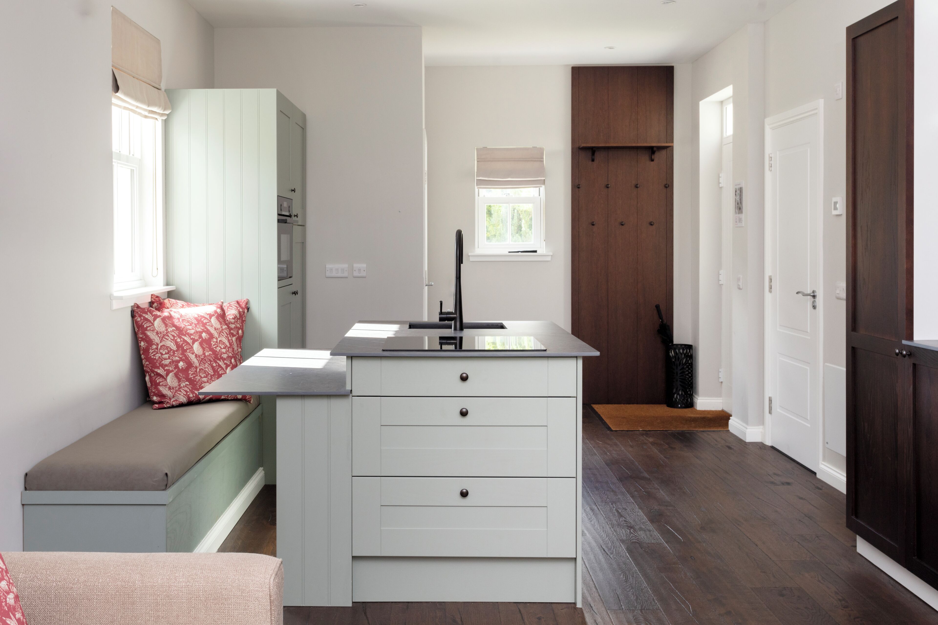 A compact kitchen with a built-in bench, a window with a view, and a door leading to another room.