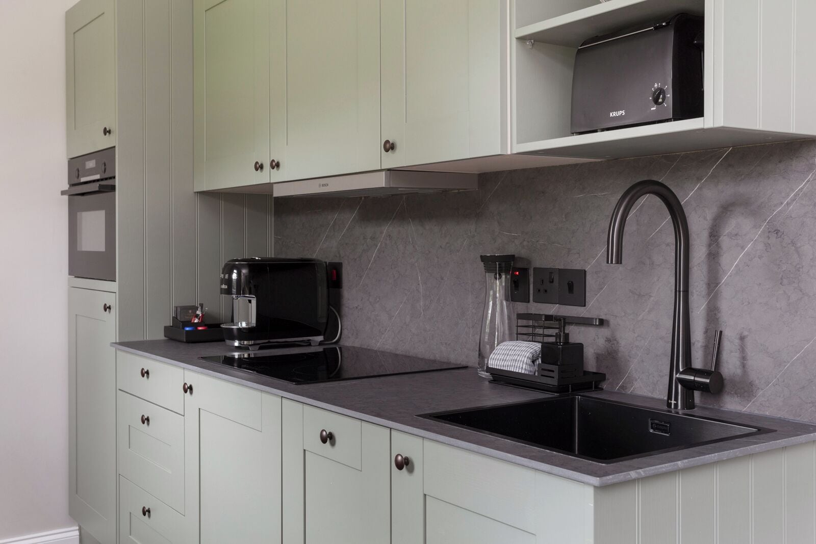 A modern kitchen with a coffee machine, a sink, and a compact refrigerator.