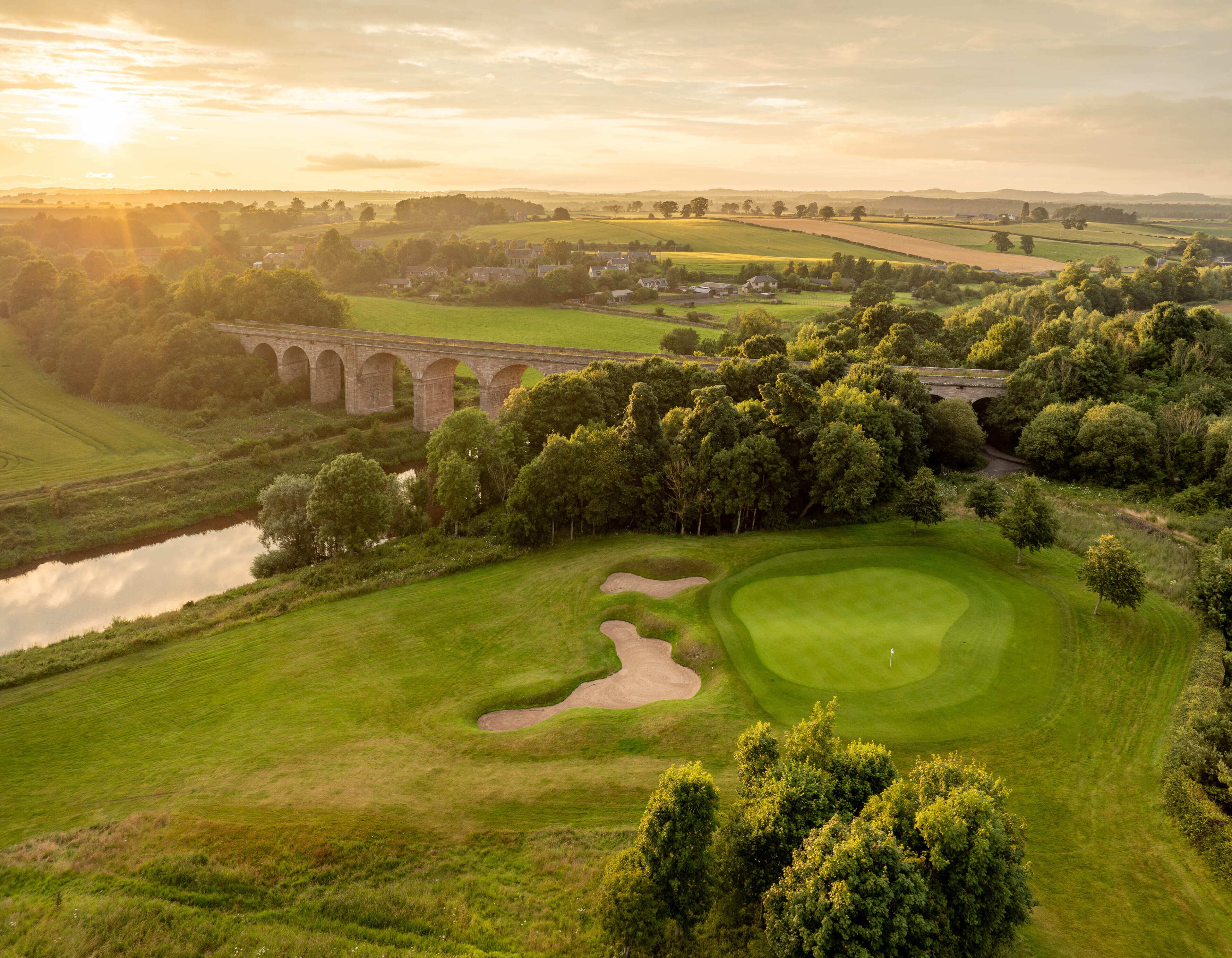 A golf course with a bridge, water body, and surrounding greenery.