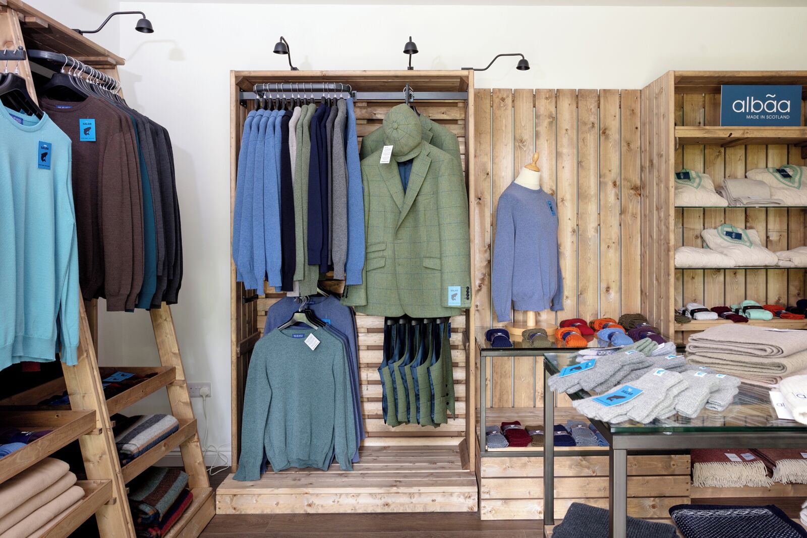 Een kledingwinkel met rekken vol overhemden en truien, een etalageman en planken met opgevouwen kleding.