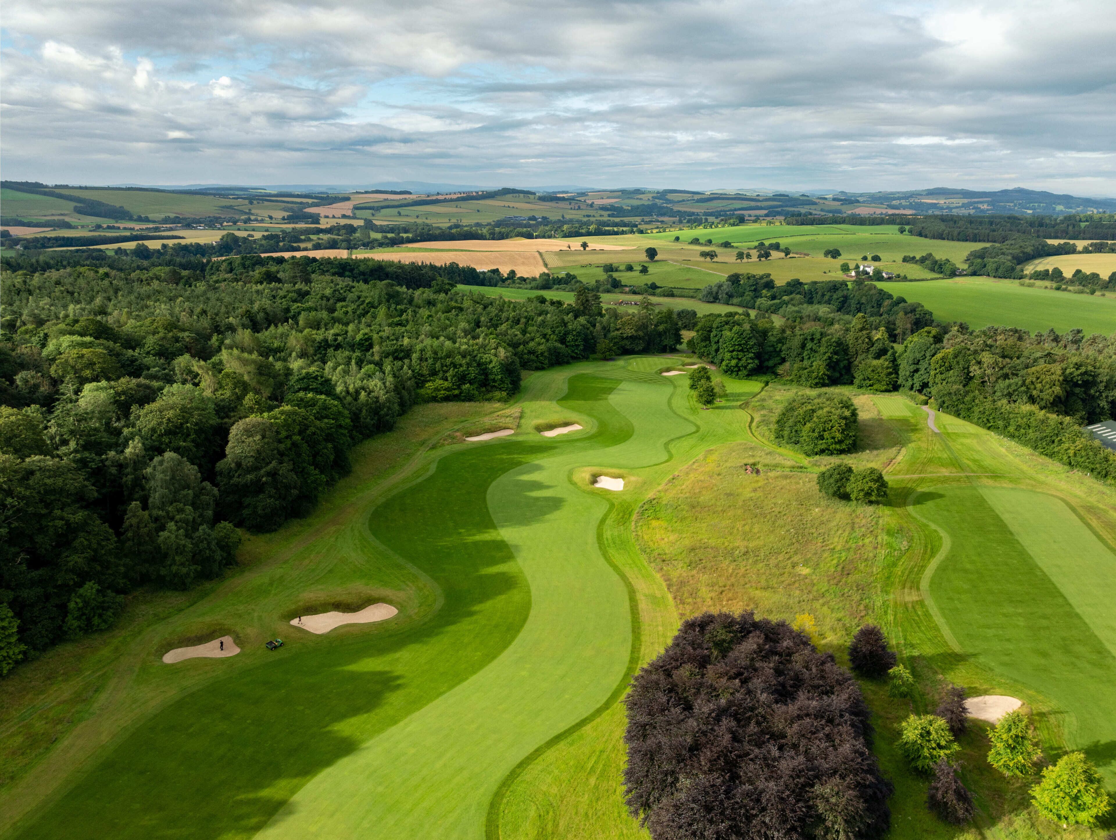 A golf course with sand bunkers, a pond, and a forested area.