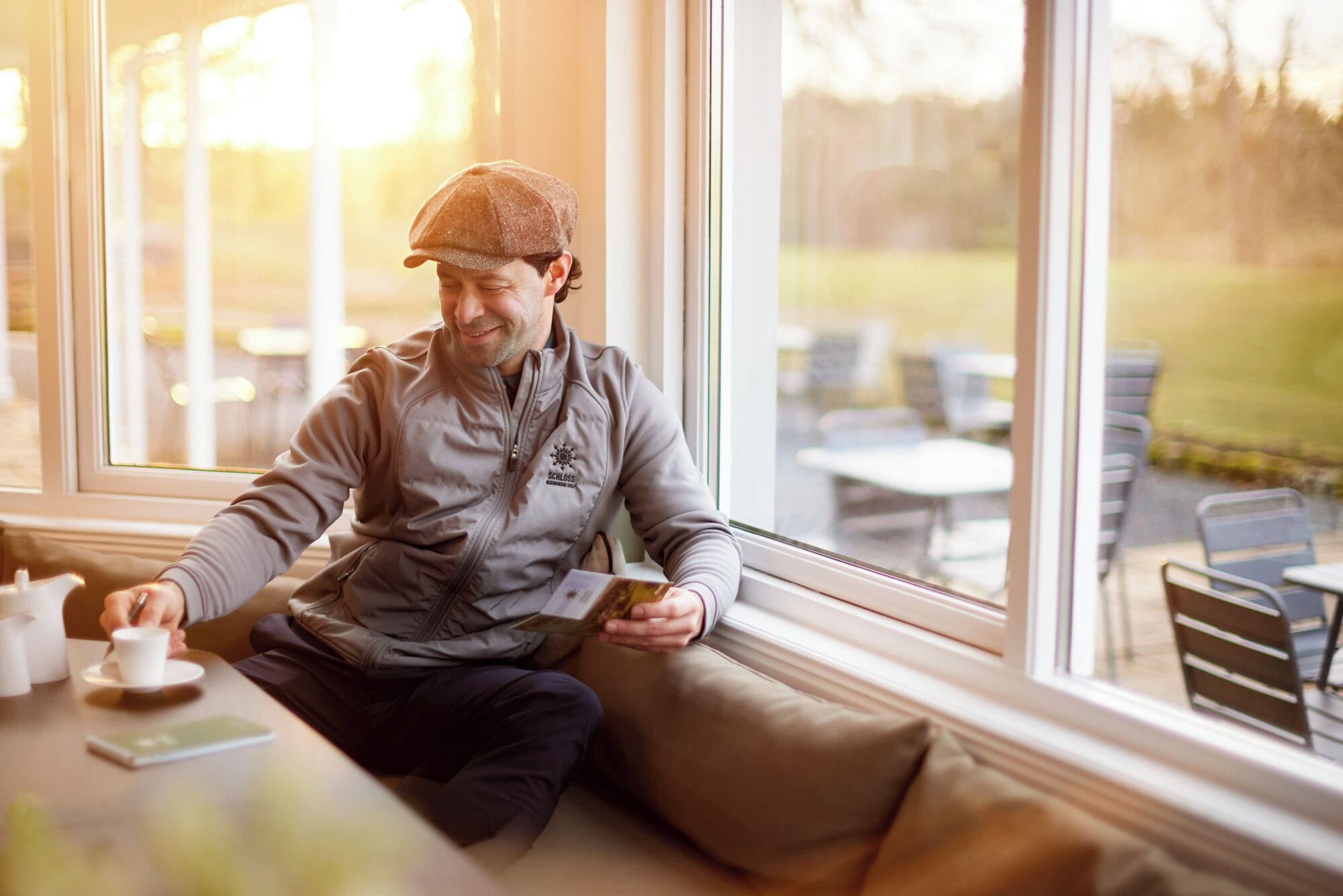 En person sidder ved et vindue med en bærbar computer, en kop og en underkop på bordet.