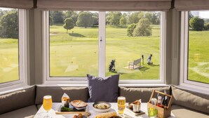 A dining area with a view of a golf course, a table with food and drinks, and a bench with a pillow. - Roxburghe Cottages, Part of Destination by Hyatt (Kelso)