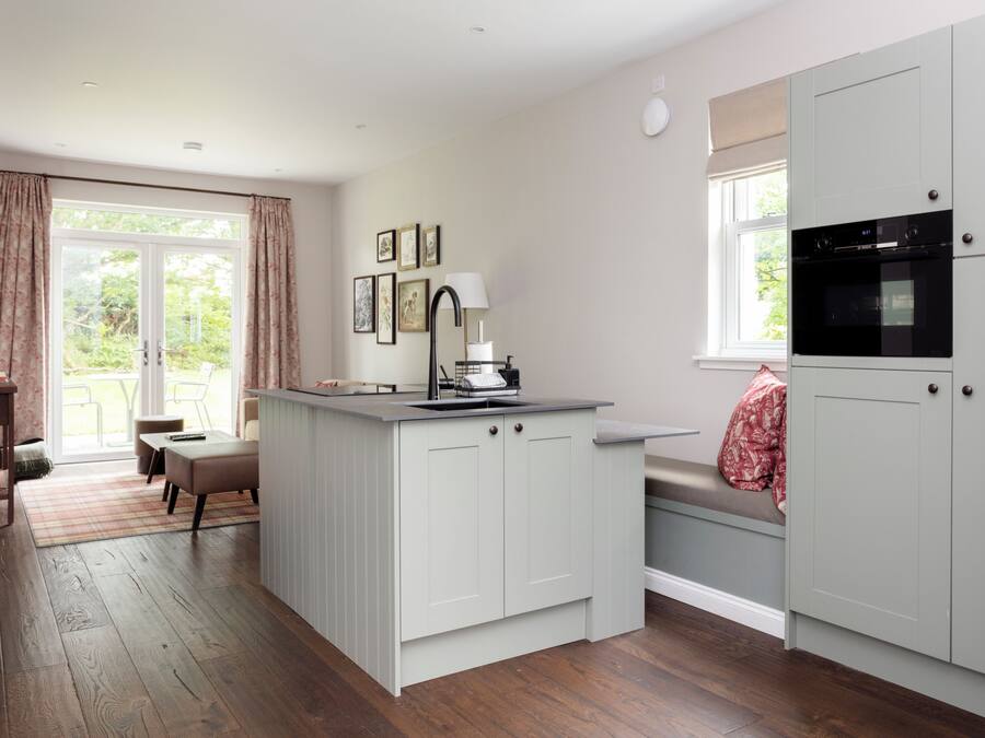 A kitchen with a central island, a dining area with a bench, and a window with curtains.