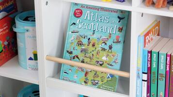 A bookshelf with a book titled 'Atlas of Scotland' by David MacPhail, surrounded by other books and colorful storage bins.