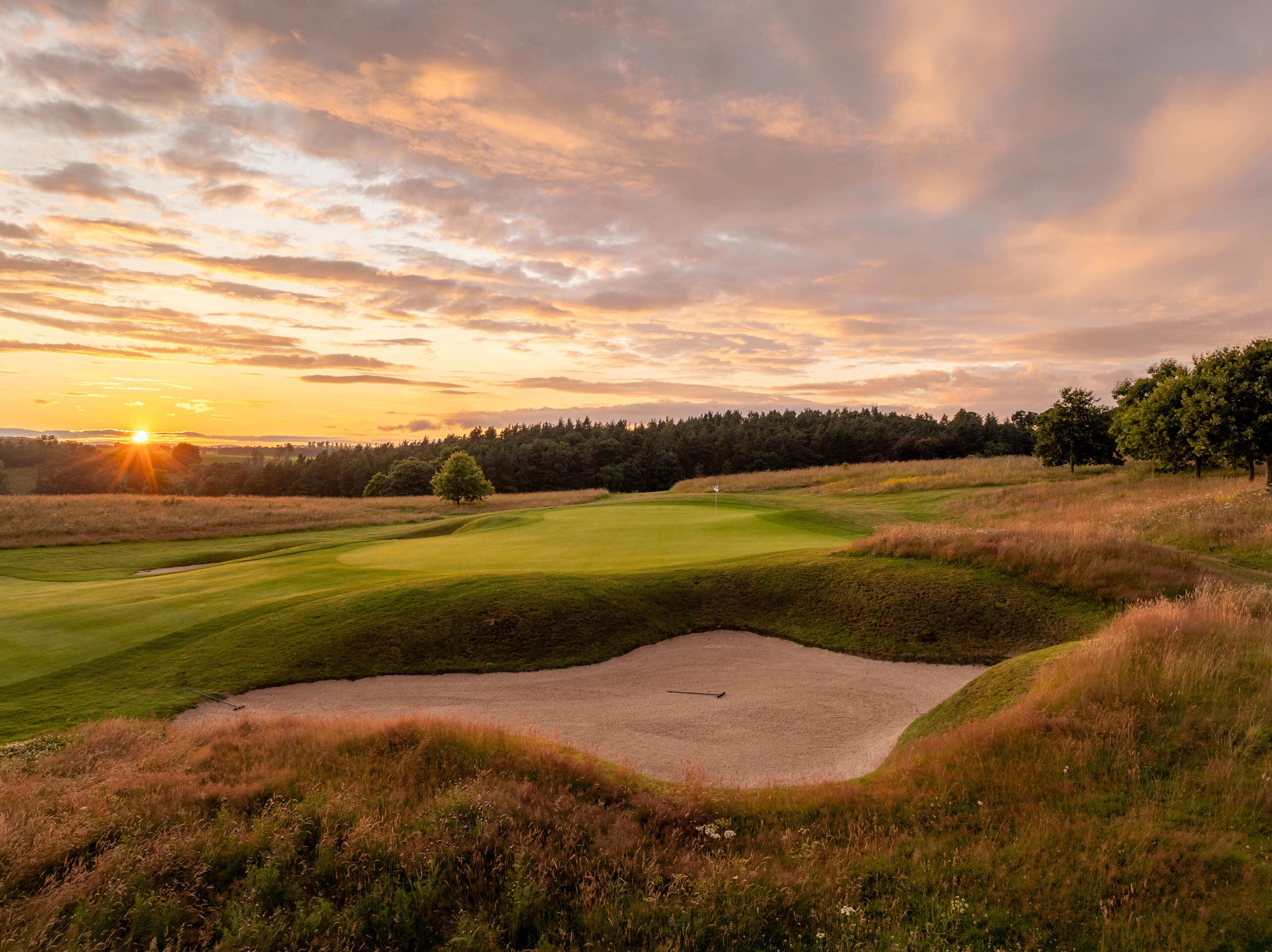 Ein Golfplatz mit Sandbunker, Bäumen und Sonnenuntergang.