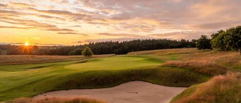 Ein Golfplatz mit Sandbunker, Bäumen und Sonnenuntergang.