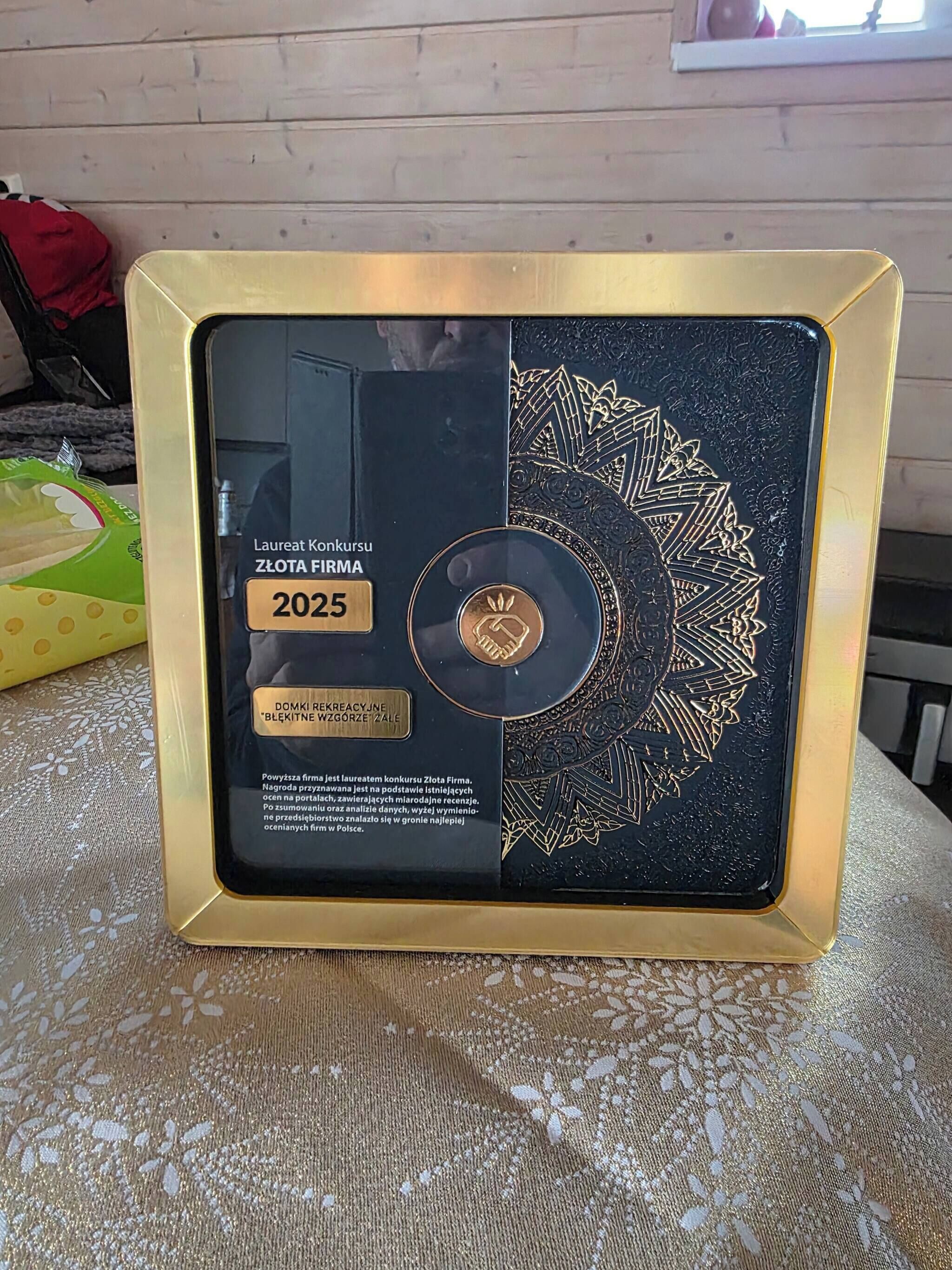 A framed certificate with a black and gold design, placed on a table.