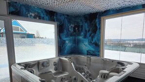 A hot tub with a view of a snowy landscape and a blue mural on the wall. - Domek nr 3 "błękitne Wzgórze" (gmina Brzuze)