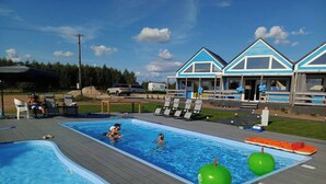 A swimming pool with a wooden deck, lounge chairs, and inflatable toys. - Domek nr 3 "błękitne Wzgórze" (gmina Brzuze)