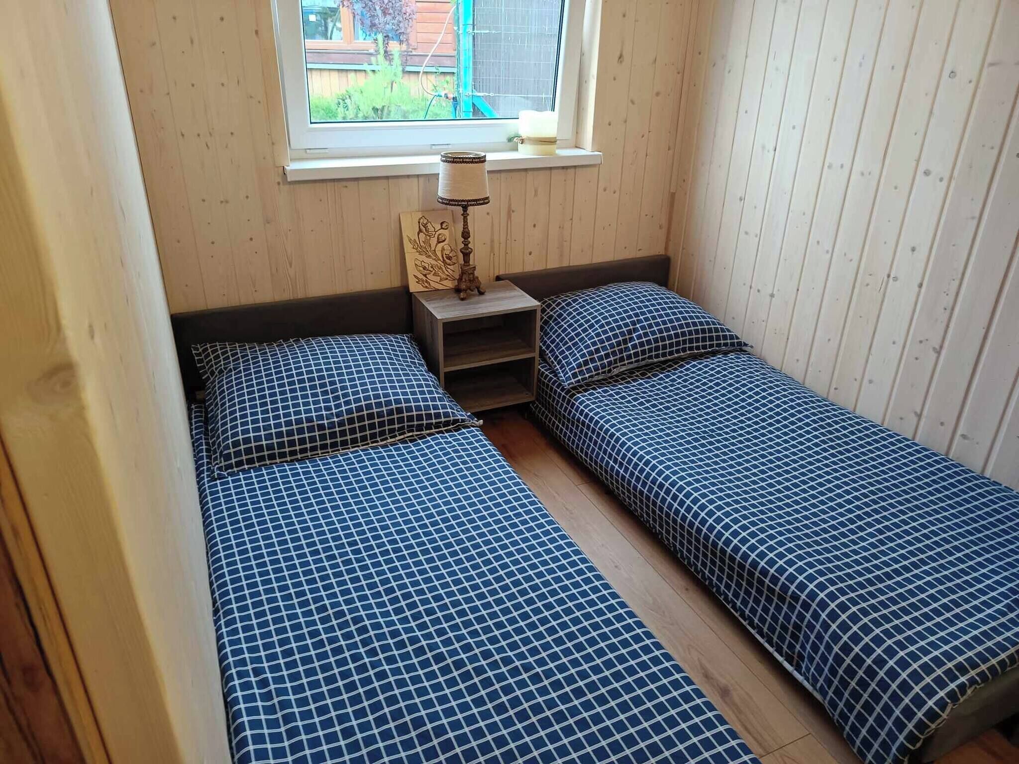 Una habitación pequeña con dos camas individuales, una mesita de noche, una lámpara y una ventana con vistas al exterior.