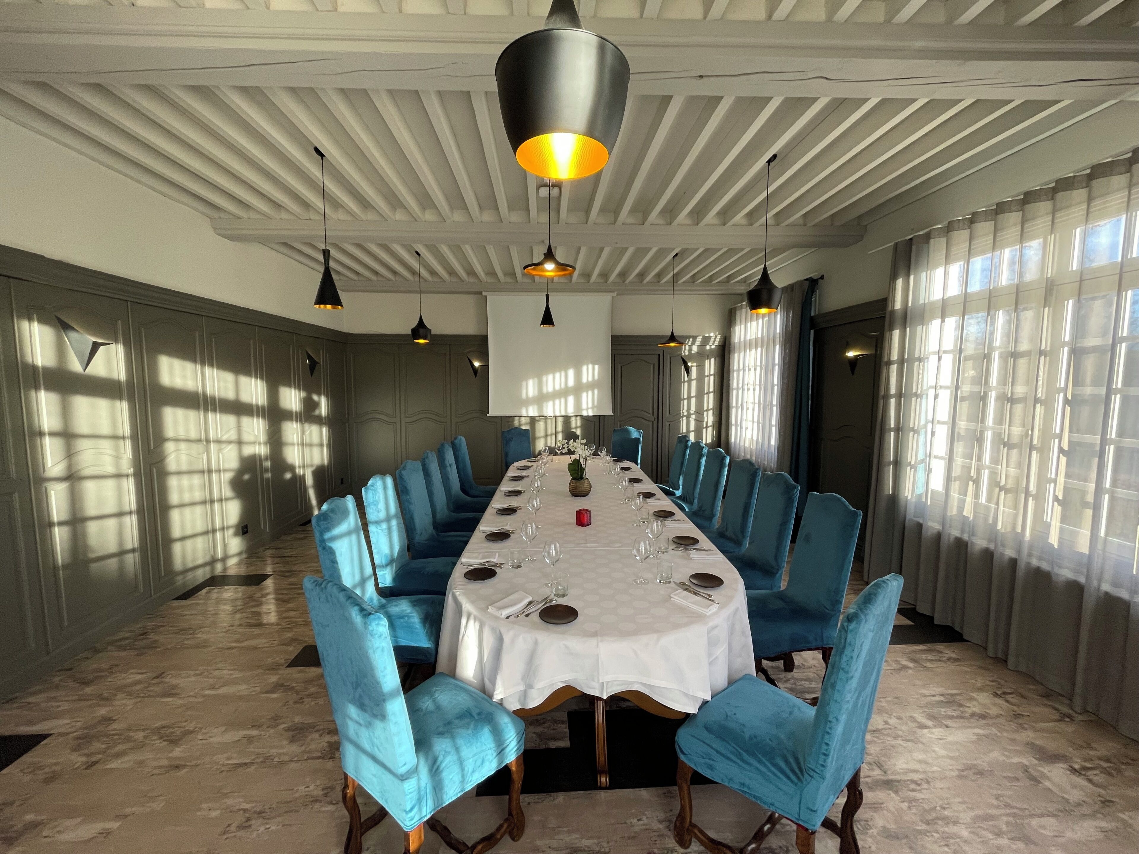 A dining room with a long table, blue upholstered chairs, pendant lighting, and a white ceiling.