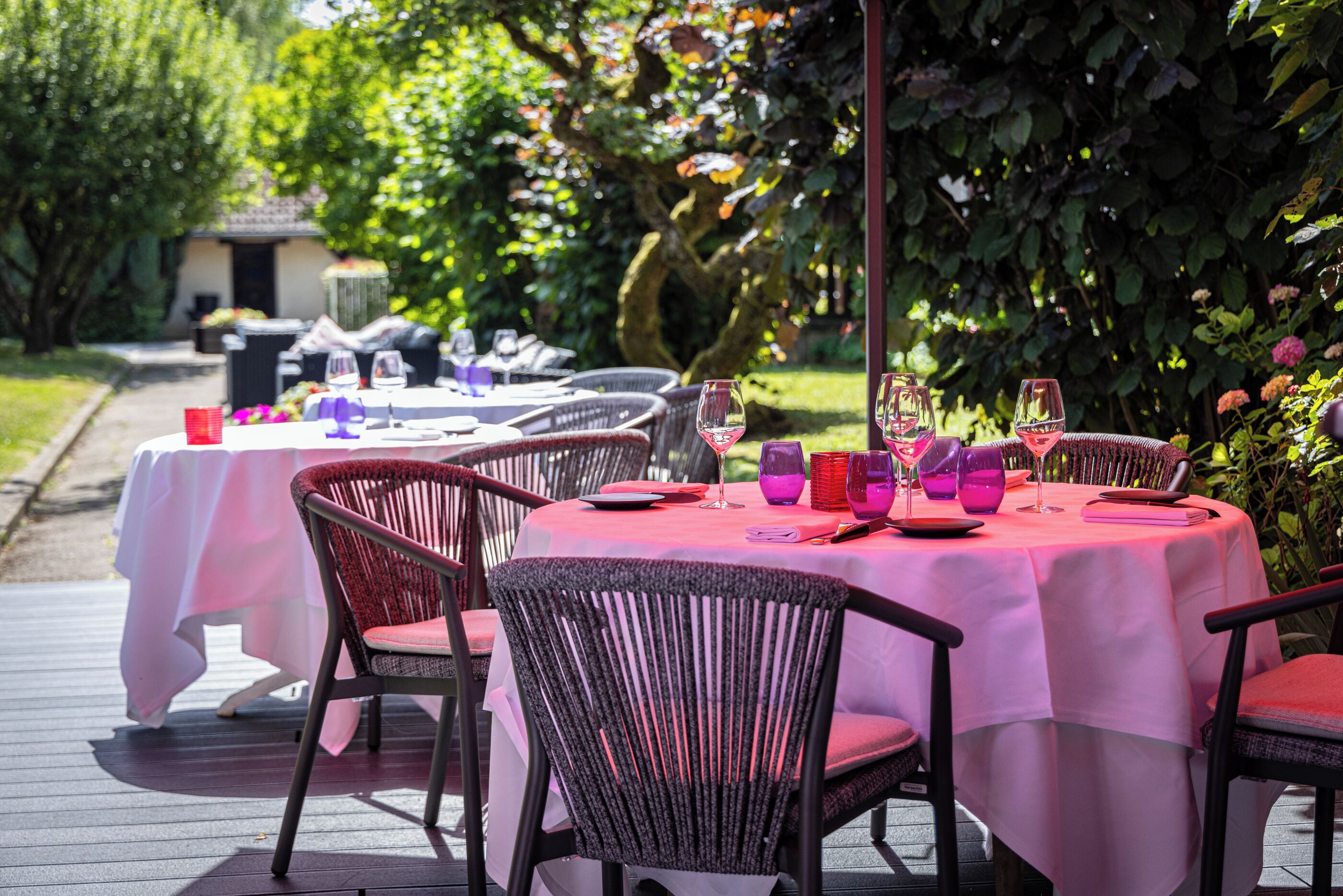 Un espace extérieur aménagé pour les repas, avec des tables rondes et des chaises en osier, le tout entouré de verdure.