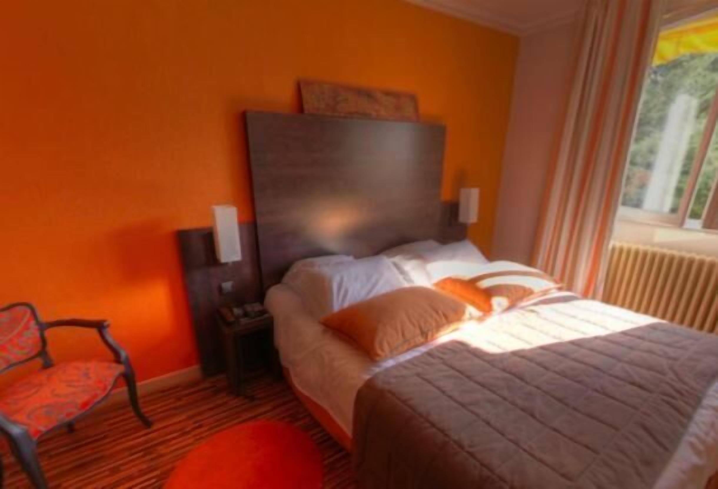 A hotel room with a bed, a nightstand, a chair, and a window with curtains.