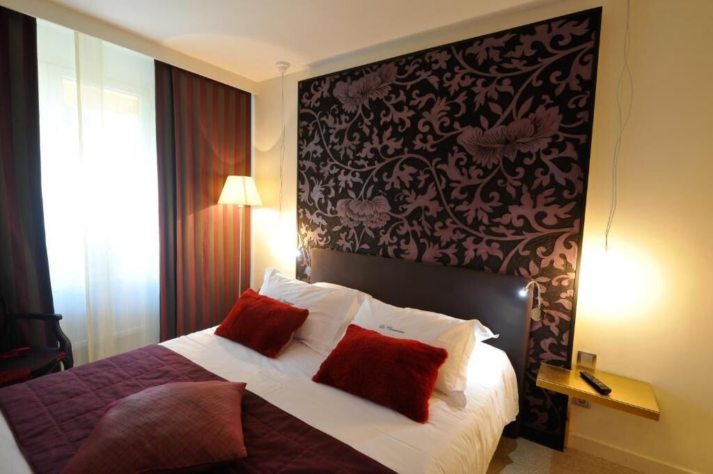 A hotel room with a bed, red pillows, a nightstand, a lamp, and a floral-patterned headboard.
