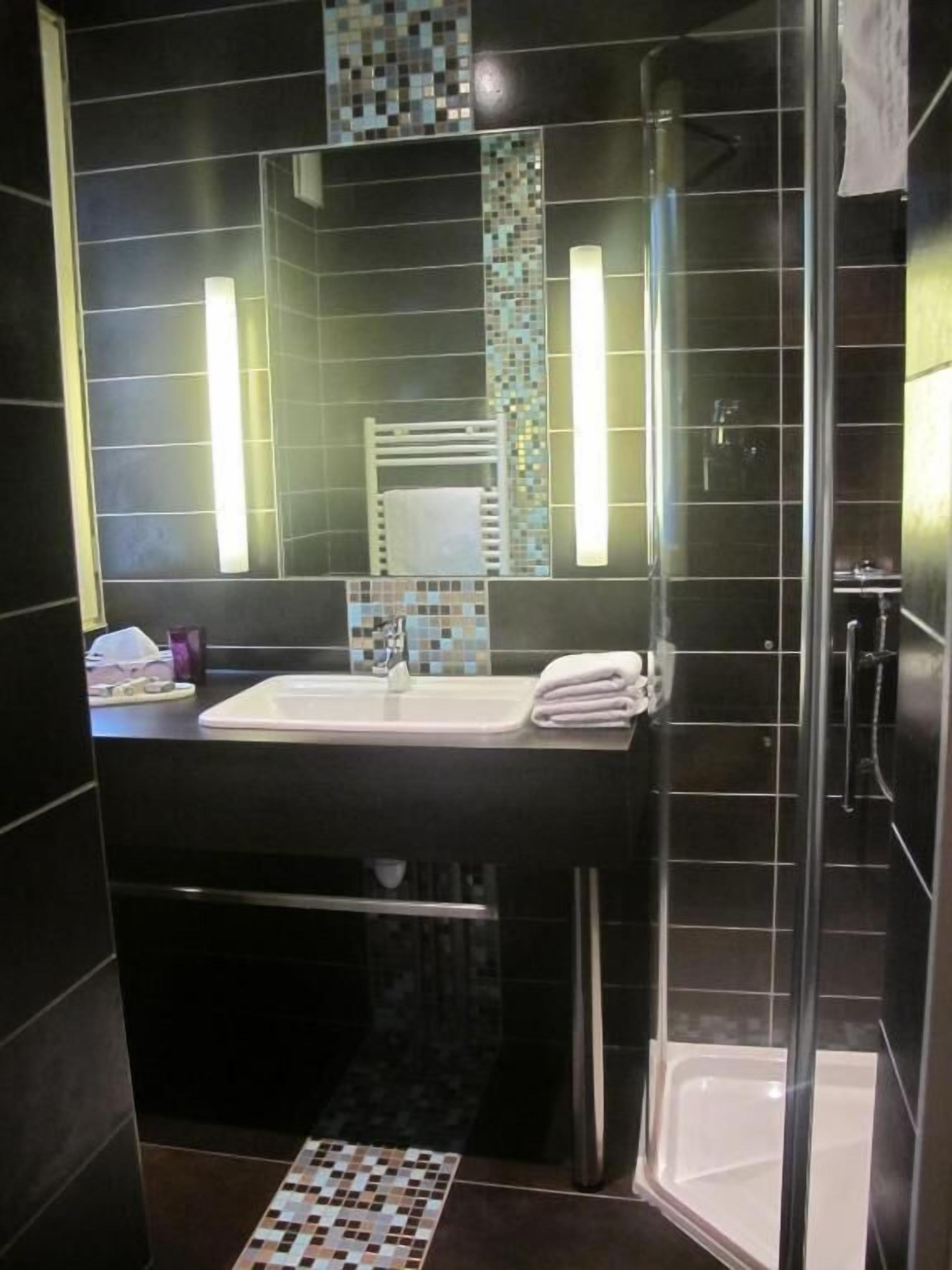 A modern bathroom with a glass shower enclosure, a sink with a mirror, and a tiled floor.