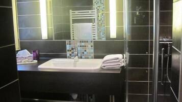 A modern bathroom with a glass shower enclosure, a sink with a mirror, and a tiled floor.