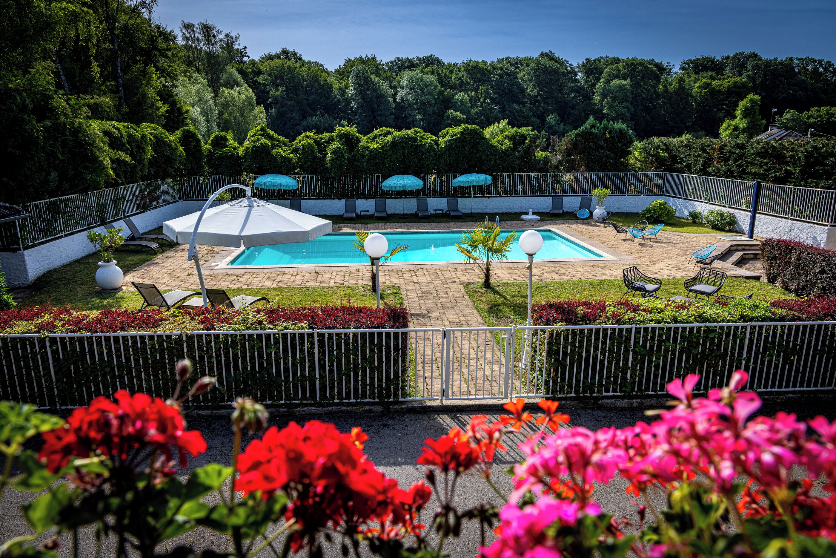 A pool area with two pools, lounge chairs, umbrellas, and a fenced garden.