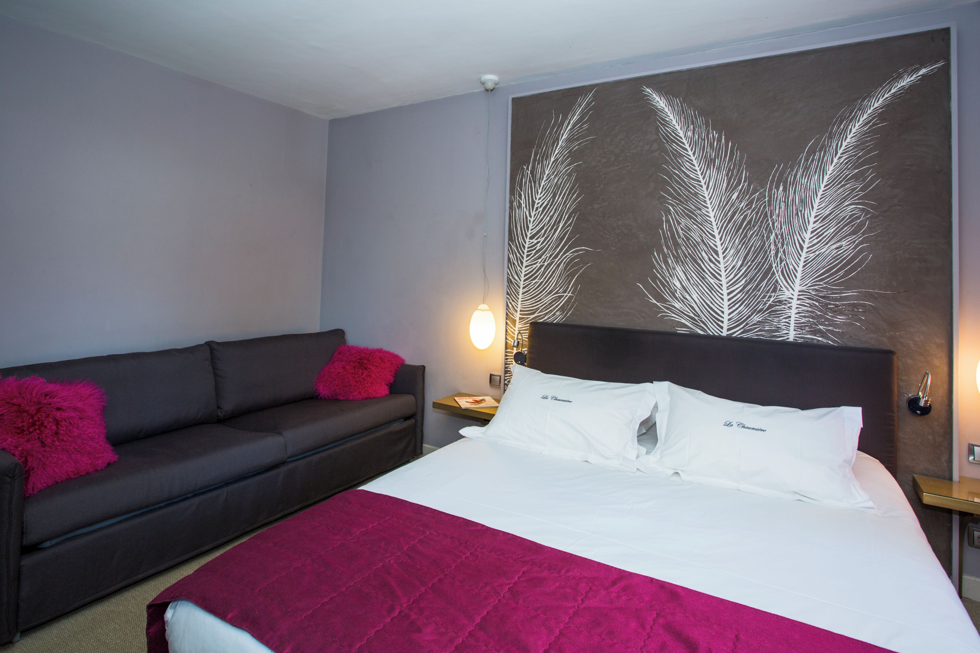 A hotel room with a bed, a sofa, a nightstand, and a wall art piece.