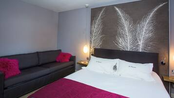 A hotel room with a bed, a sofa, a nightstand, and a wall art piece.