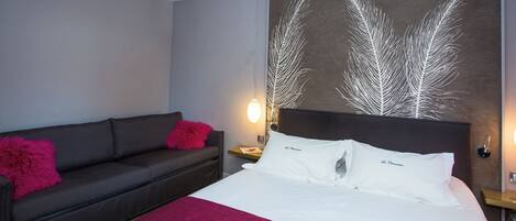 A hotel room with a bed, a sofa, a nightstand, and a wall art piece.