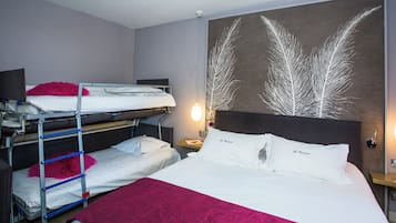 A hotel room with bunk beds, a large bed, a nightstand, a wall-mounted lamp, and a decorative wall piece.
