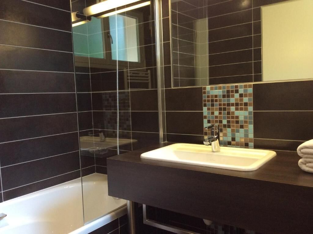 A modern bathroom with dark tiles, a white sink, and a glass shower enclosure.