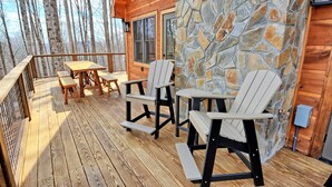 Una terraza de madera con sillas Adirondack, una mesa y un muro de piedra.