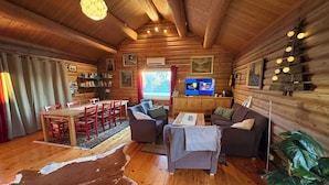 Ein Holzblockhaus-Innenraum mit Essbereich, Sofa, Fernseher und Bücherregalen.