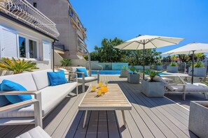 A poolside area with a white sofa, lounge chairs, and umbrellas. - Stylish vacation apartment in Crikvenica with pool (Crikvenica)