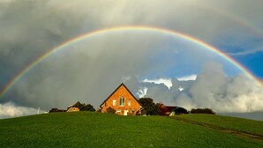 Une maison située sur une colline verdoyante, avec un arc-en-ciel qui la surplombe.
