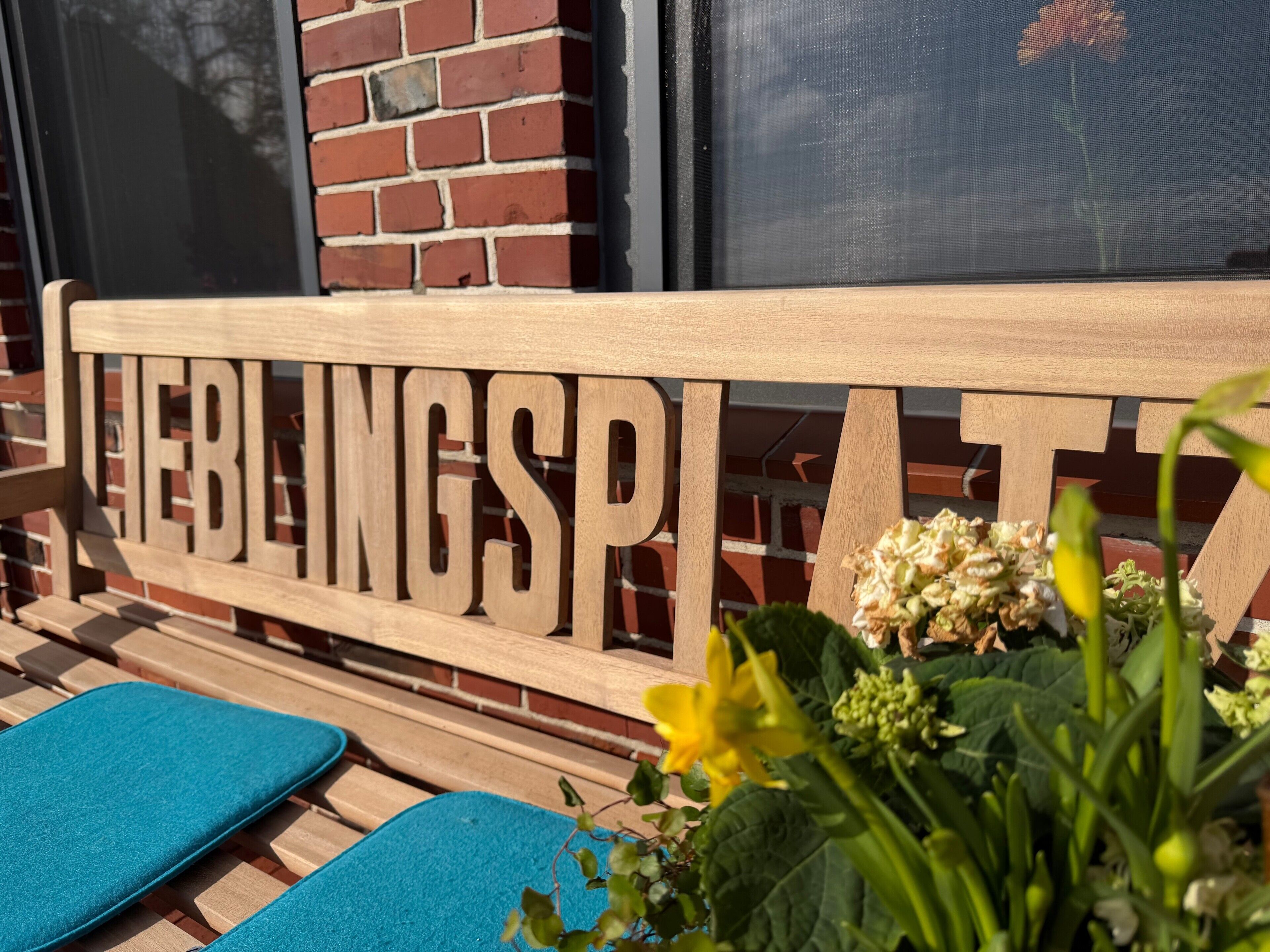 A wooden bench with the words 'HELBINGSPA' carved into it, a brick wall, and a window in the background.