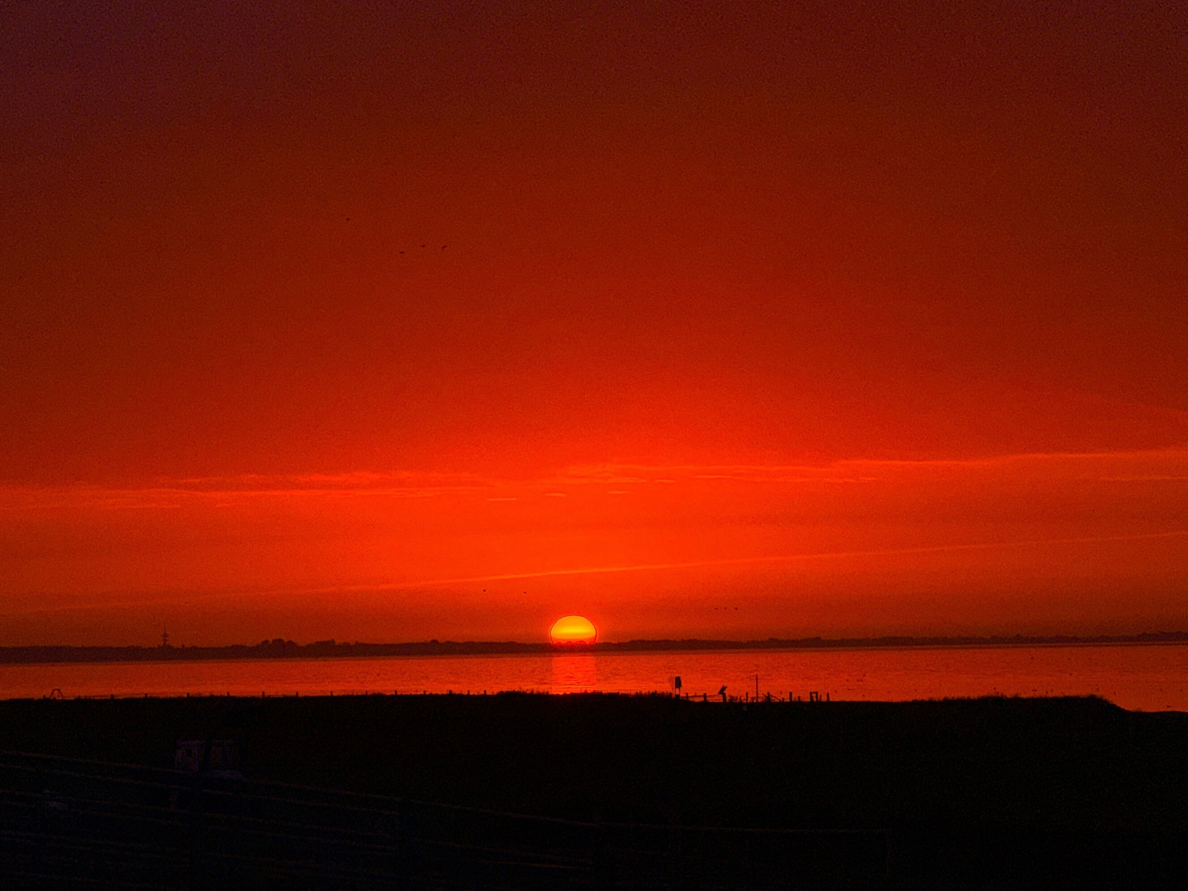 Auringonlasku veden äärellä, taustalla rannikon siluetti.