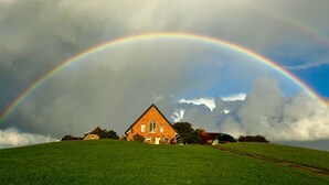 Una casa su una collina erbosa con un arcobaleno nel cielo.