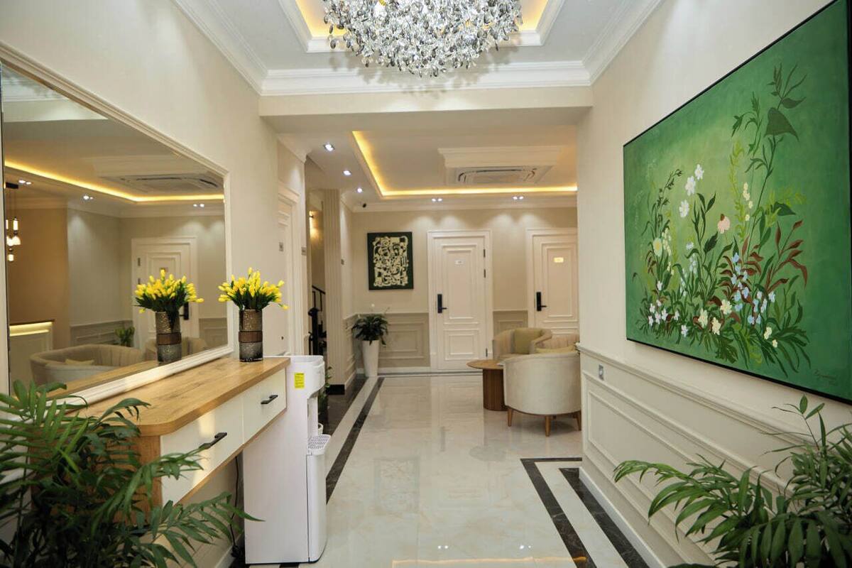 A hotel lobby with a large mirror, a chandelier, a painting, and a reception desk.