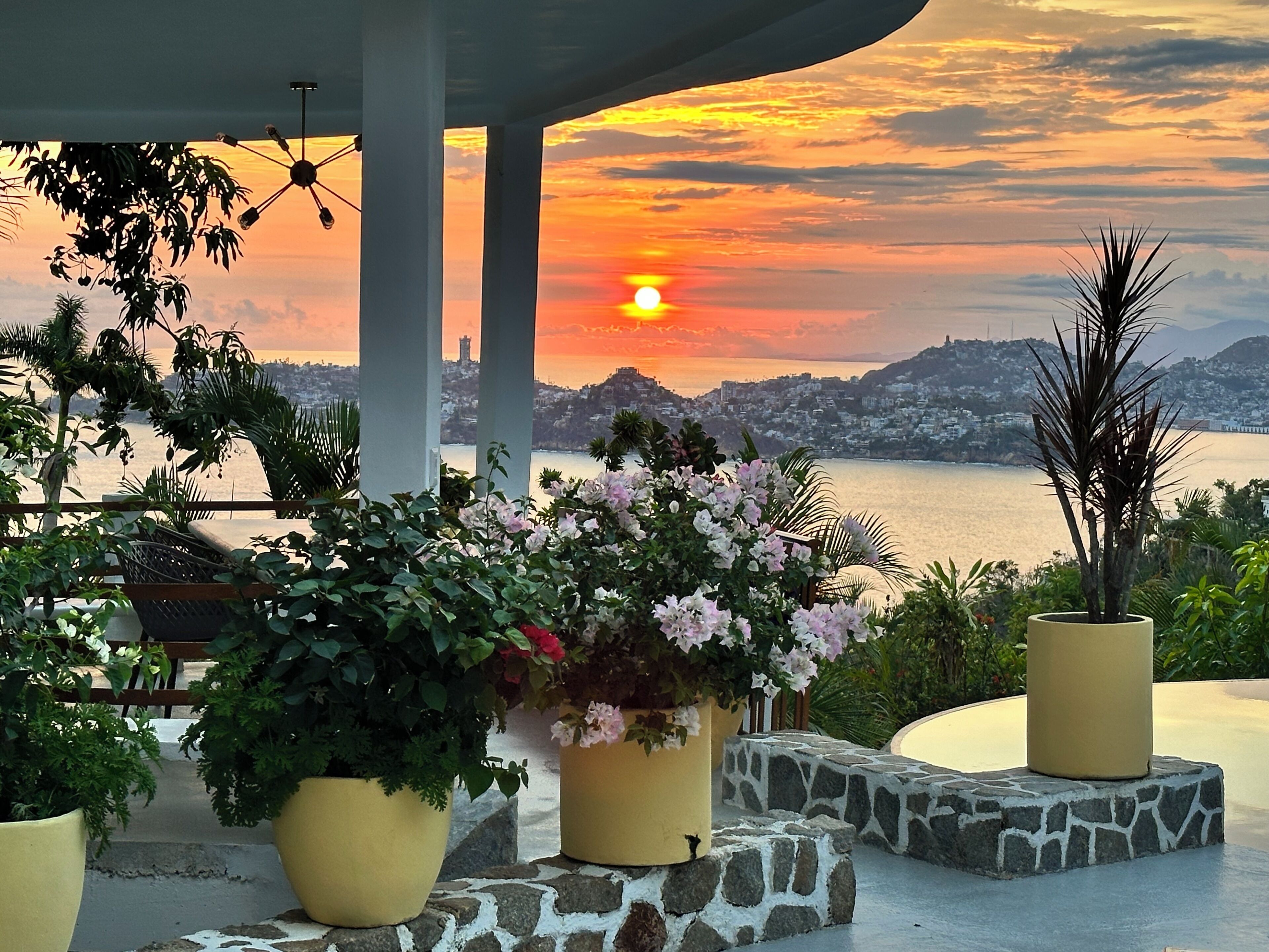 A sunset view from a covered outdoor area with potted plants and a stone pathway.