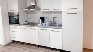 Una cocina moderna con armarios blancos, una campana extractora de acero inoxidable, horno empotrado, cafetera y fregadero.