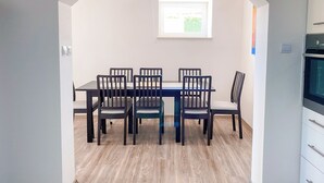 Un comedor con una mesa rectangular y seis sillas, un arco de entrada, una ventana con vistas a la vegetación y una cocina con estufa.