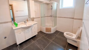 Un baño moderno con ducha de vidrio, lavamanos blanco con espejo y un inodoro.