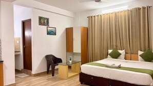 A hotel room with a bed, a desk, a chair, a wardrobe, and a door. - HOTEL MELVET RESIDENCY (Kanayannur)